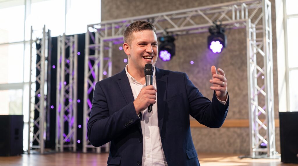 Spreker met microfoon voor een verlicht podium