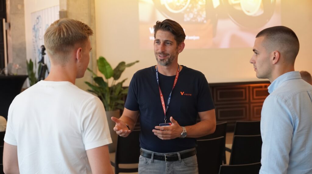 Coach in Vesto-shirt in gesprek met twee deelnemers tijdens een netwerkmoment